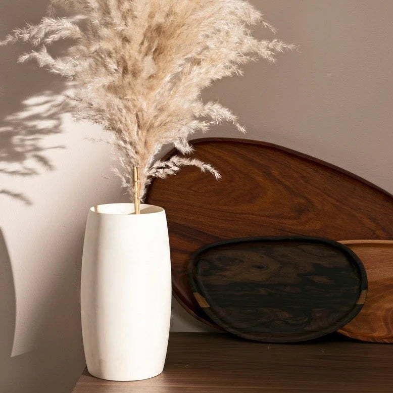 White vase with dried pampas grass against a neutral wall with wooden elements.