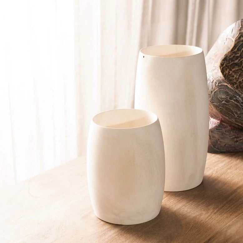 Two white ceramic vases on a wooden surface with a soft, blurred background