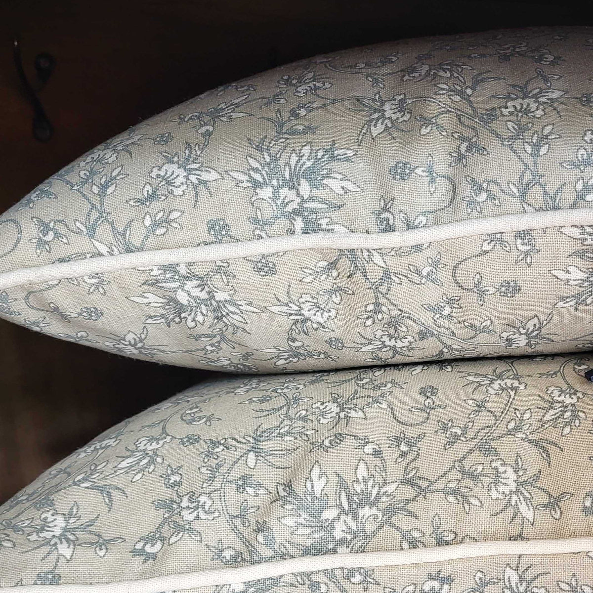 Two floral-patterned pillows on a wooden shelf with a tag.