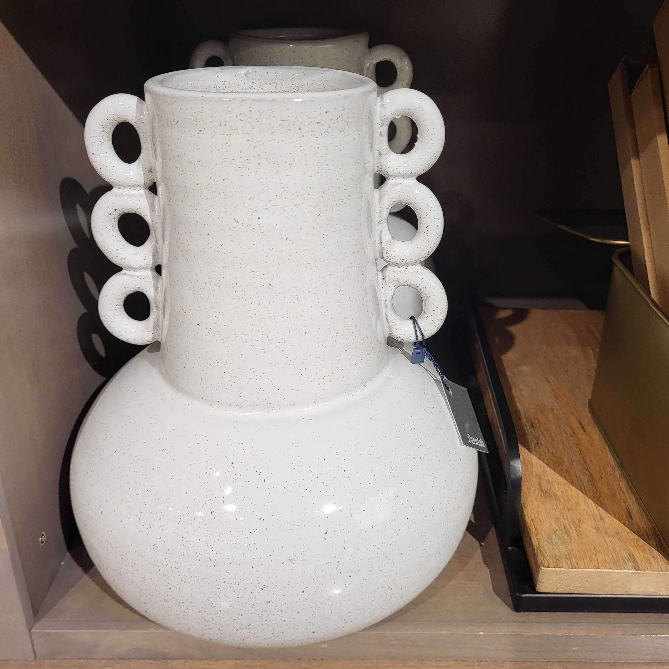 White vase with circular handles on a shelf