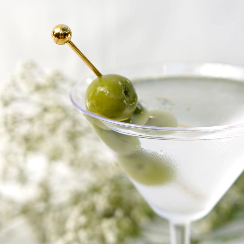 Martini glass with a olive on a toothpick against a blurred floral background