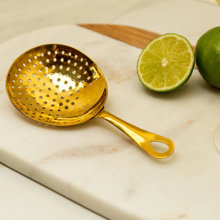 Gold strainer on a marble surface with limes