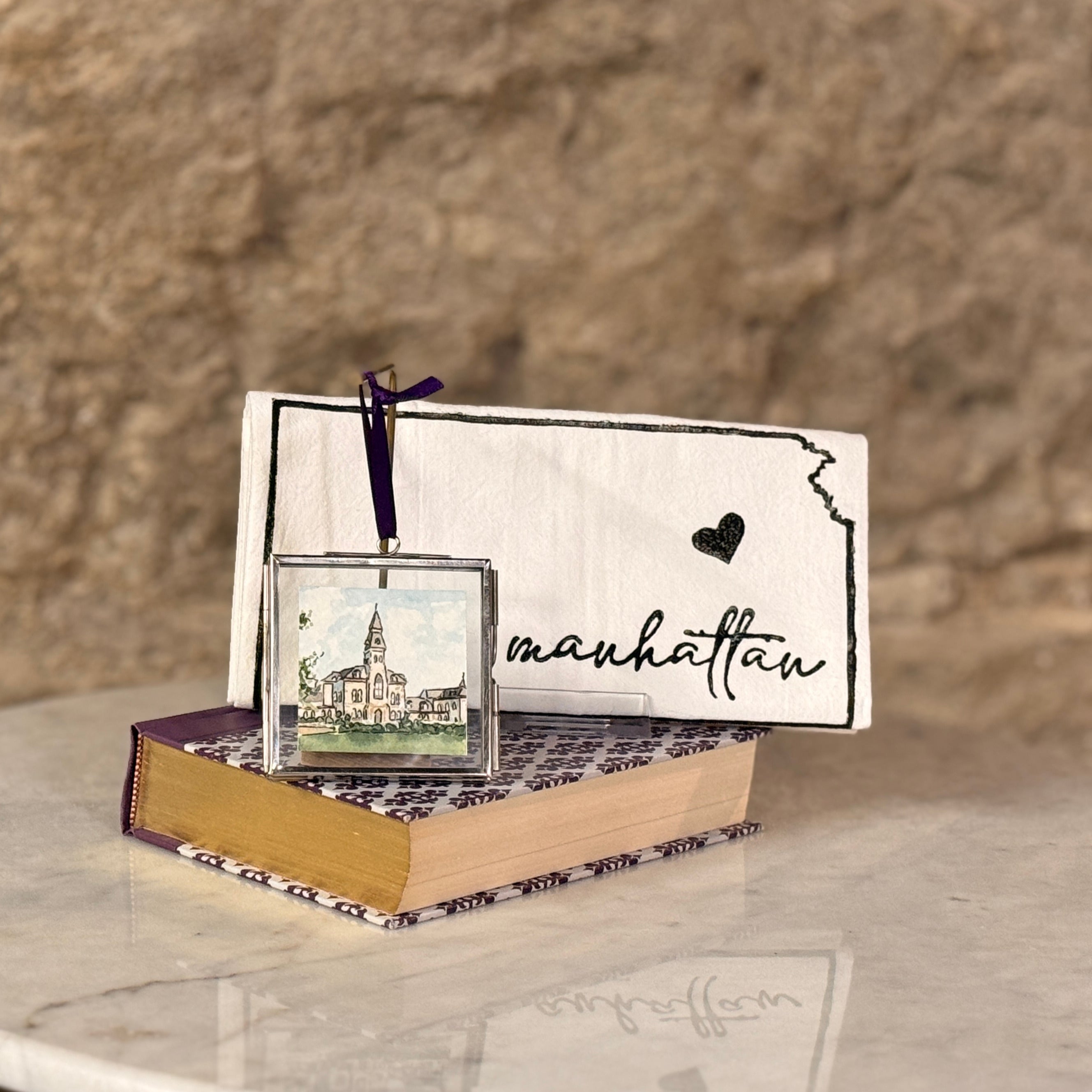 Decorative book with a small framed picture and 'Manhattan' text against a stone wall background