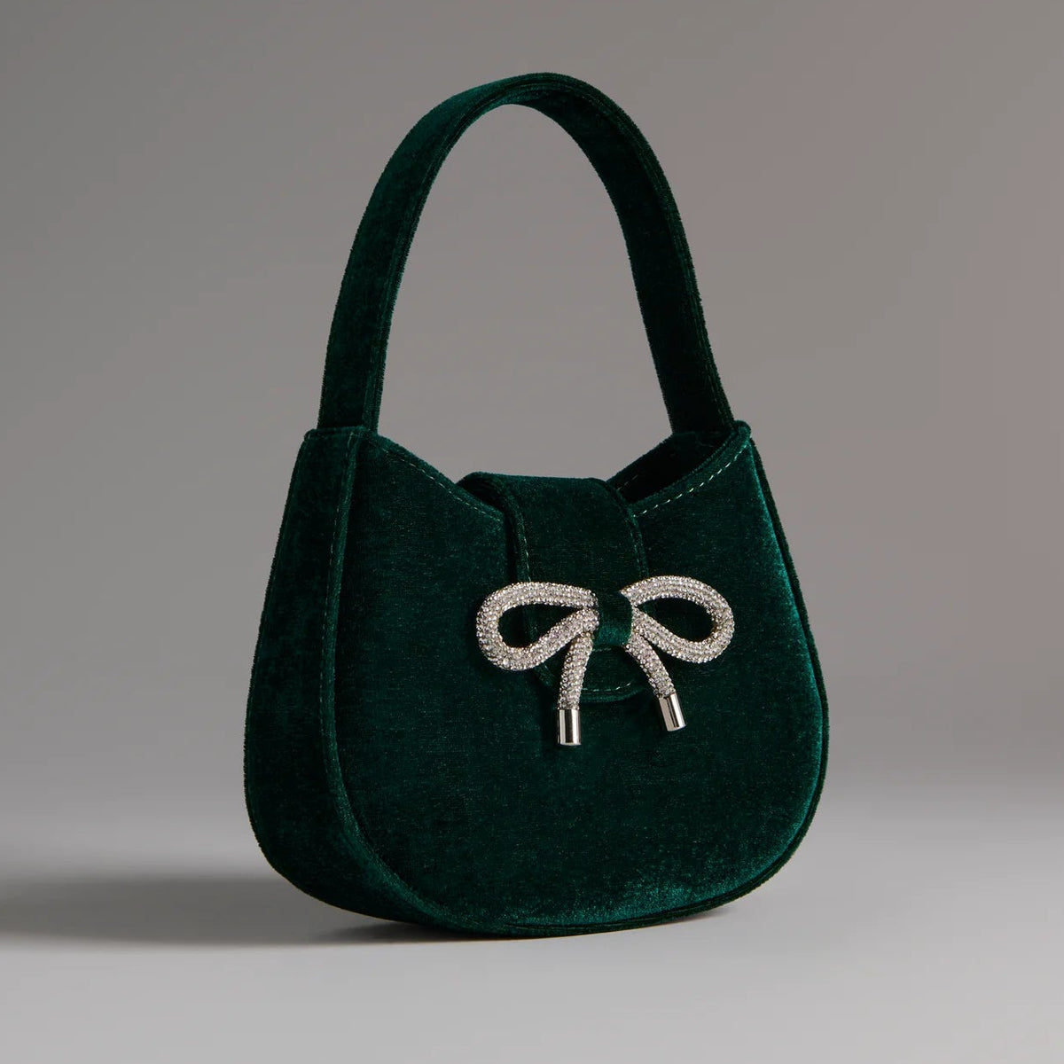 Green velvet handbag with a bow detail on a gray background
