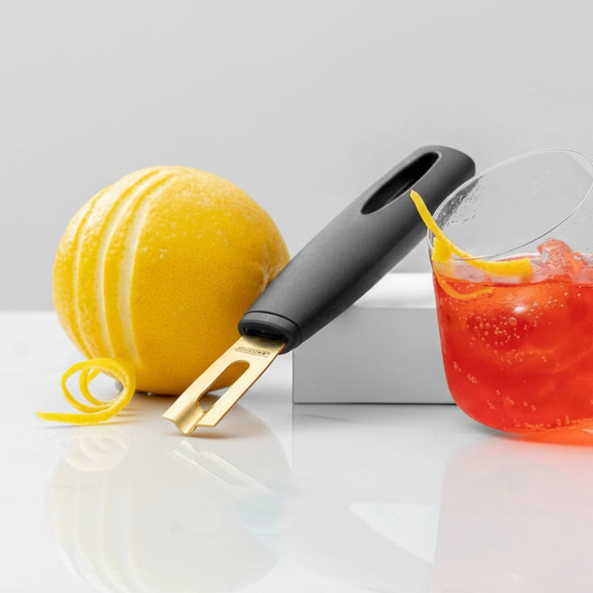 Lemon peeler with a lemon and a cocktail in the background, featuring text about the blade size.