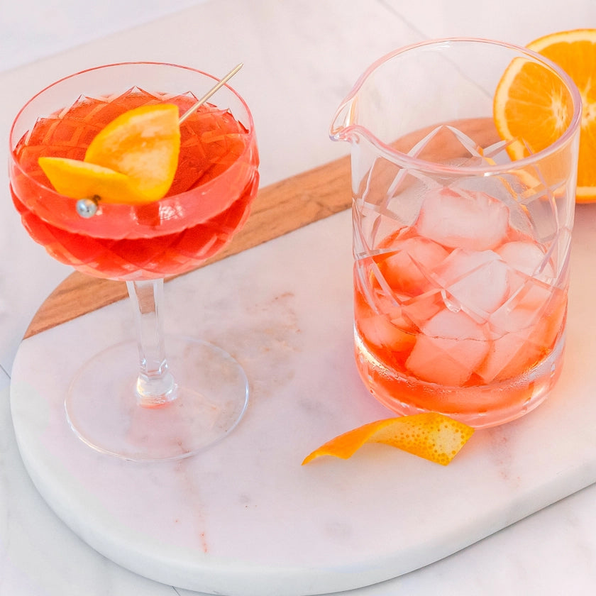Cocktail with lemon garnish and a glass of pink cocktail with ice on a marble surface.