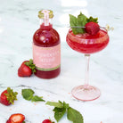 Strawberry gin bottle and cocktail with strawberries and mint leaves on a marble surface