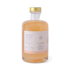 Clear bottle with peach-colored liquid and gold cap on a white background