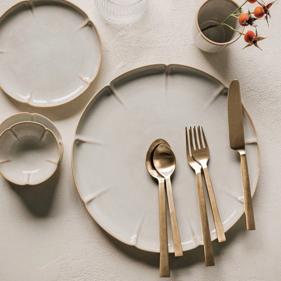 Dinnerware set with plates, cutlery, and a small cup on a textured surface.