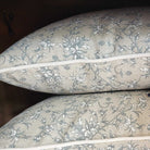 Two floral-patterned pillows on a wooden shelf with a tag.