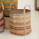 Three woven baskets with striped patterns on a light surface, with a plant in the background.