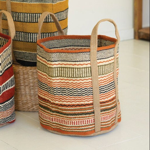 Three woven baskets with striped patterns on a light surface, with a plant in the background.
