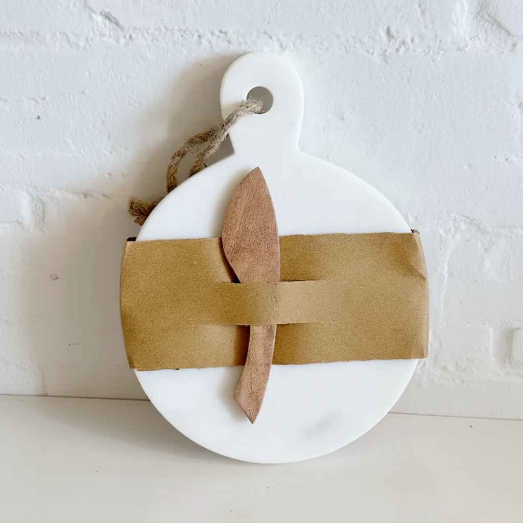 White marble cutting board with a wooden knife wrapped in brown paper on a white background