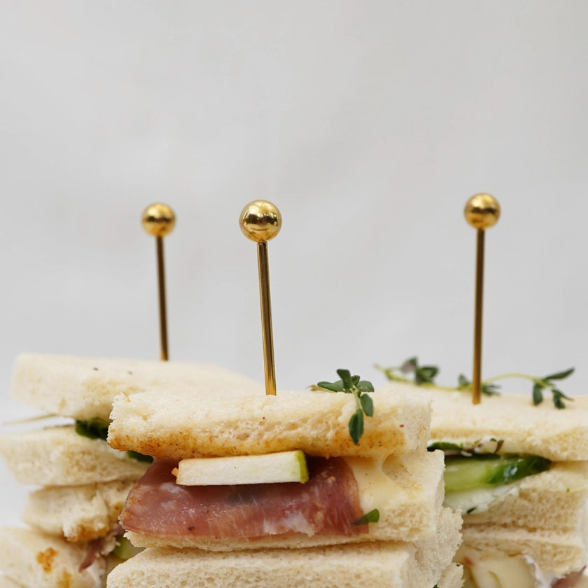 Small sandwiches with gold toothpicks on a light background