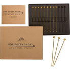 Gold cocktail picks in a black box with a cardboard packaging labeled 'One Dozen Short Cocktail Picks' on a white background.