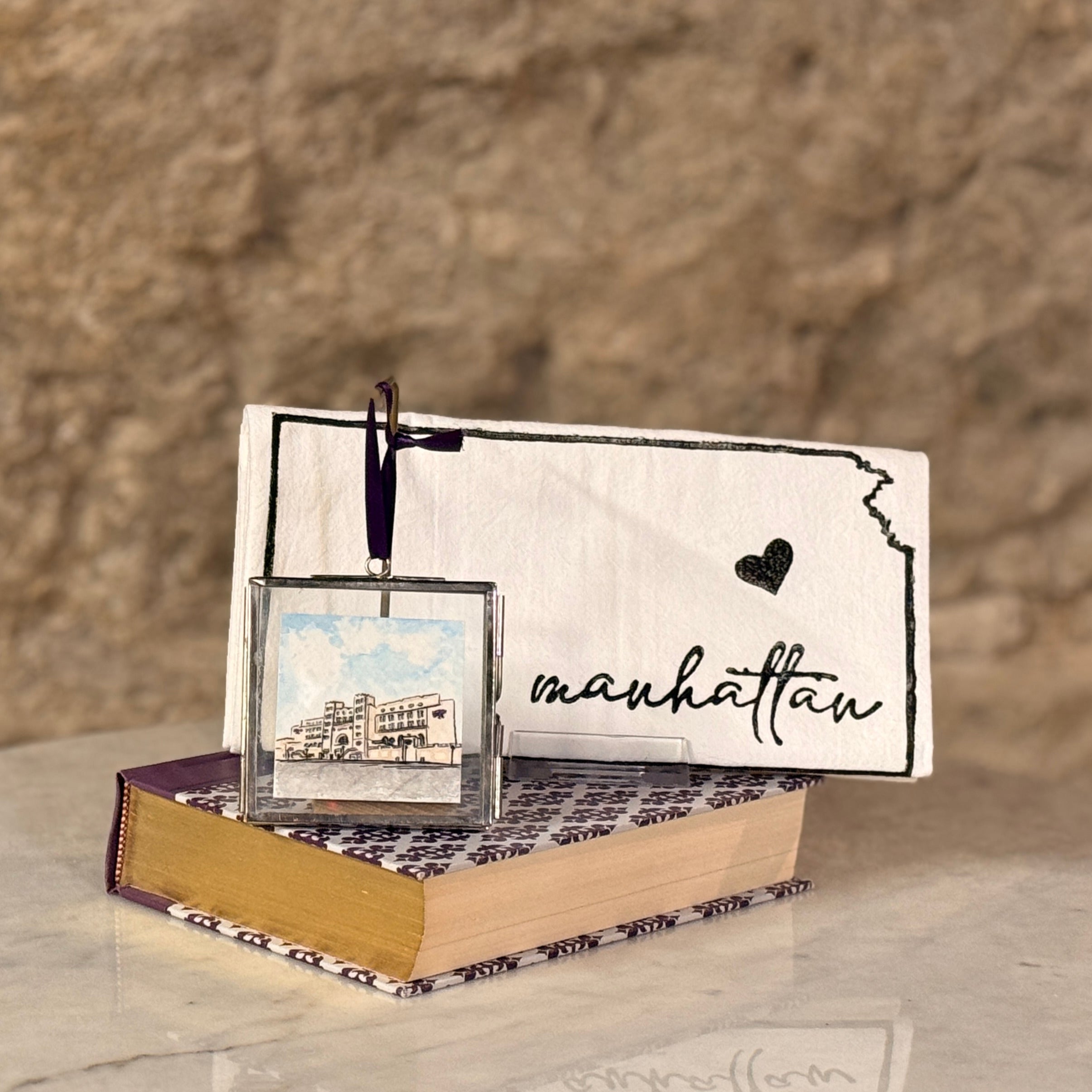 Decorative book with a small framed picture and 'Manhattan' sign on a textured surface