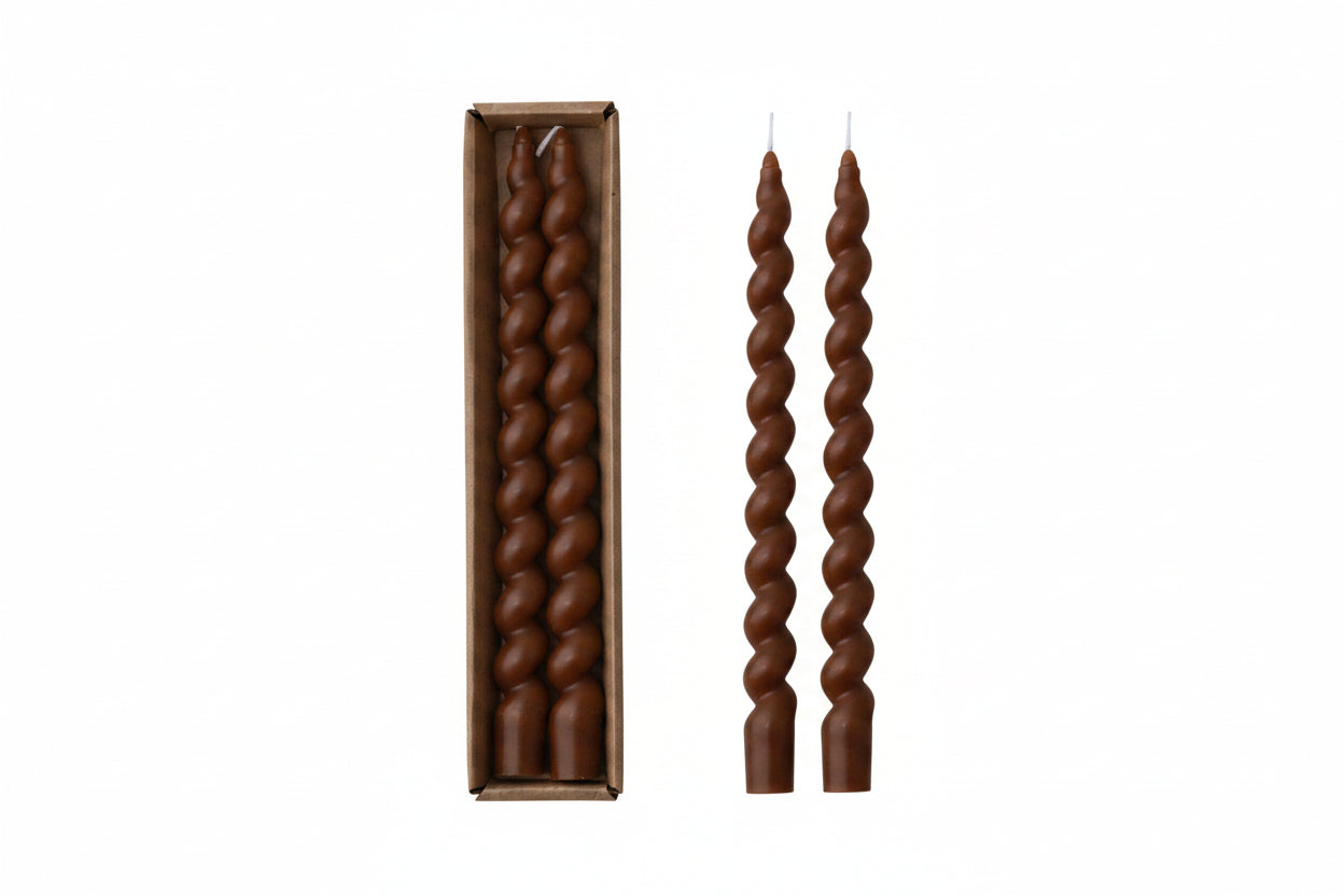 Two twisted candles next to an open box containing more candles on a white background