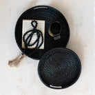 Black woven basket with a tassel, book, and cup on a light background