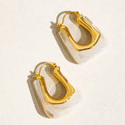 Gold hoop earrings with clear acrylic accents on a light beige background