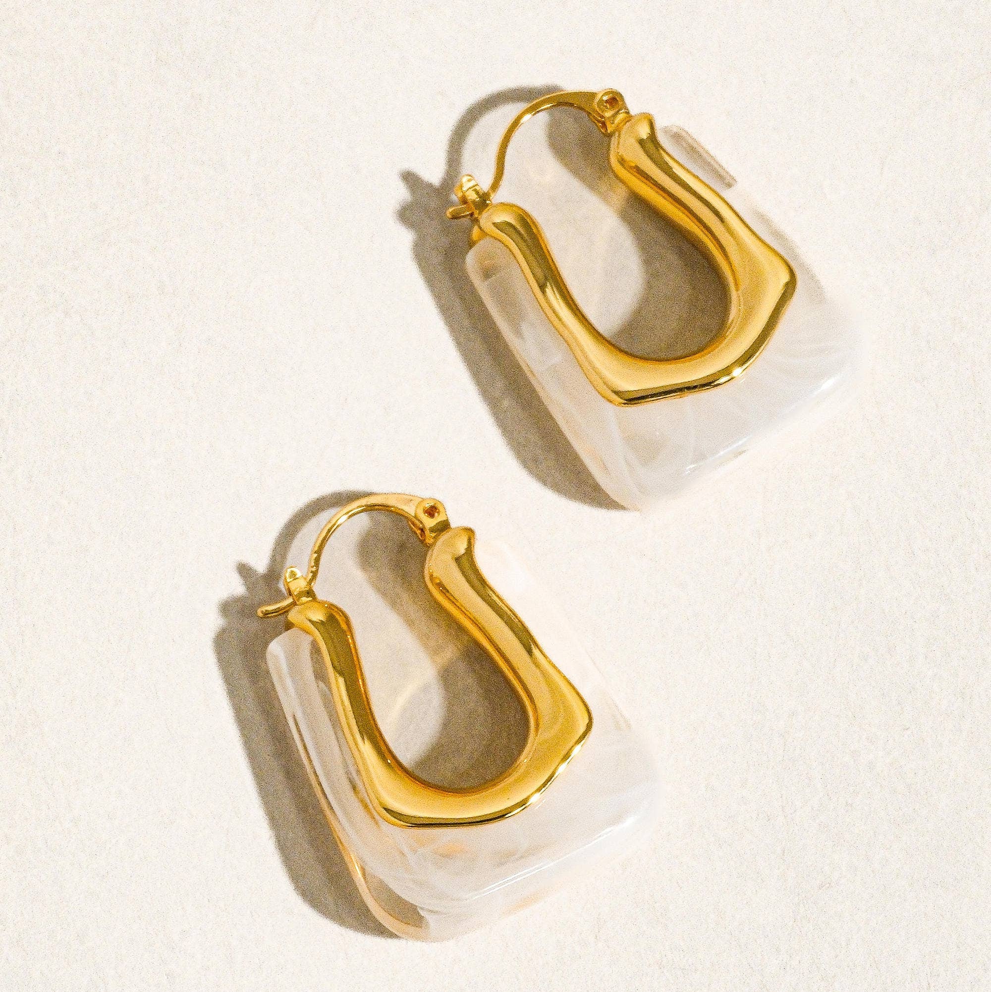 Gold hoop earrings with clear acrylic accents on a light beige background